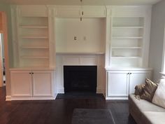 an empty living room with built in bookshelves and a couch next to the fireplace