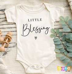 a baby bodysuit with the words little blessing printed on it next to some toys