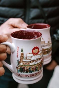 two coffee mugs with pictures on them are being held by someone's hands