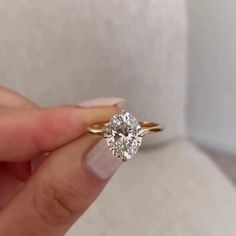 a woman's hand holding an engagement ring with a diamond in the center, on top of a white surface