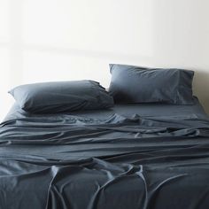 an unmade bed with blue sheets and pillowcases on it in a white room