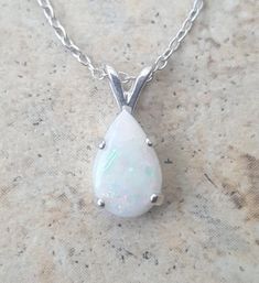 This lovely Opal drop necklace is Sterling Silver with an approx. 1 ct genuine Australian Opal, prong set in handmade settings..The Opal is a natural, AAA top quality Opal and exhibits good fire.The setting is hand made by me and is a strong prong setting which keeps the Opals in securely. The Opal Necklace is approx. 1/2 long. (from the top of the bale to the bottom of the stone.)The chain is a durable cable chain and looks great with the Opal pendant.Opal is the birthstone for October.Please n White Teardrop Jewelry With Prong Setting, White Round Drop Necklace For Anniversary, White Oval Necklace With Prong Setting, White Drop Solitaire Necklace Classic Style, Drop White Solitaire Necklace For Formal Occasions, White Pendant Necklace With Bail, White Drop Solitaire Necklace Gift, White Teardrop Solitaire Necklace For Formal Occasions, Classic Oval Drop Necklace Gift