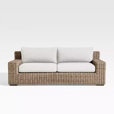 a wicker couch with white pillows on it's back and side ends, facing the camera