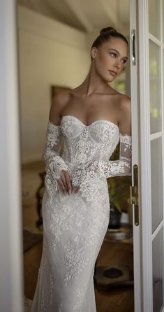 a woman in a white wedding dress is standing by the door and looking at the camera