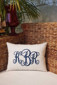 the monogrammed pillow is sitting on a wicker chair next to a potted plant