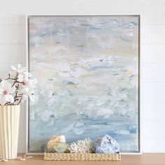 a vase with flowers and rocks on a table next to a painting in the background