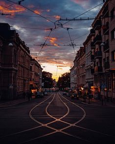 an empty street with some buildings and wires above it at sunset or dawn in the city