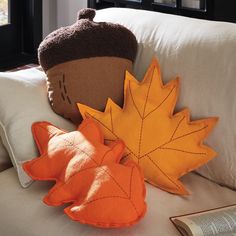 two decorative pillows sitting on top of a white couch next to an orange and brown leaf