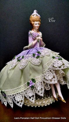 a figurine is sitting on a table wearing a dress with laces and flowers