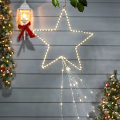 a lighted star hanging from the side of a house next to christmas trees and wreaths