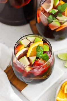 a person holding a glass with some fruit in it on top of a cutting board