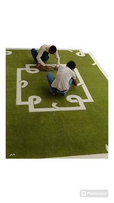 two men kneeling down on top of a green area rug with white letters and numbers