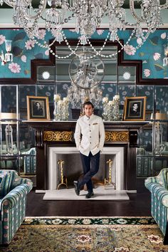 a man standing in front of a fireplace with chandelier hanging from the ceiling