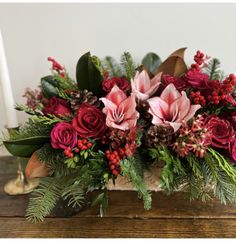 an arrangement of flowers and greenery on a wooden table next to a lit candle