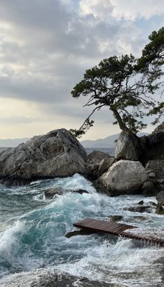 an ocean scene with waves crashing on the rocks and a lone tree in the distance