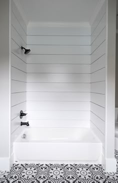 a white bath tub sitting next to a toilet in a bathroom with black and white flooring