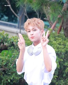 the boy is posing with his peace sign in front of some bushes and trees,