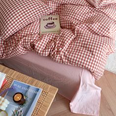 a bed with a red and white checkered comforter next to a magazine on the floor