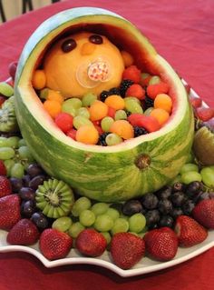 a watermelon boat filled with lots of fruit on top of a red table cloth