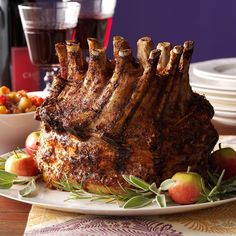 a large piece of meat sitting on top of a white plate next to apples and wine glasses