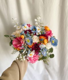 a hand holding a bouquet of flowers on top of a white cloth covered bed sheet