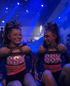 two women in black and pink outfits sitting on the floor with blue lights behind them