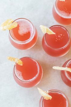 four glasses filled with red drinks and garnished with orange peels