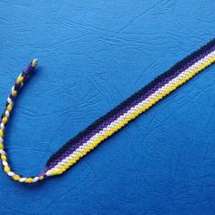 a purple, yellow and white beaded lanyard on a blue surface