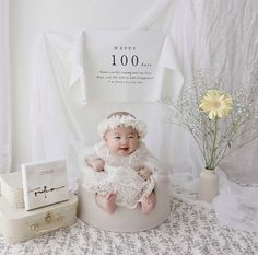 a baby is sitting in a white pot next to some flowers and a gift box