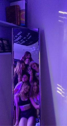 a group of young women taking a selfie in a bathroom mirror with purple lighting