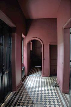 an empty hallway with black and white checkered flooring, red walls and arched doorways