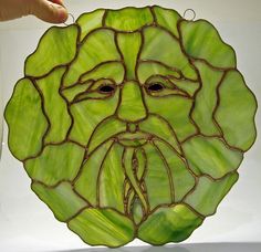 a green glass plate with a face on it's side and a hand reaching for the top