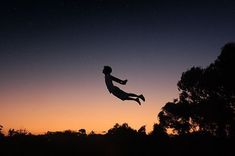 a person is flying through the air at night with trees in the foreground and stars in the sky above