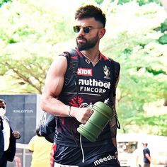 a man with sunglasses on holding a green water bottle and wearing a black vest while standing in front of a crowd