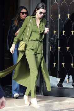 a woman in green is walking out of a building with her hand on her hip