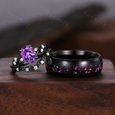 two wedding rings with purple and green stones on them sitting on top of a wooden table