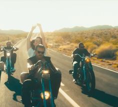 three people riding motorcycles on the road with their arms in the air and one person waving