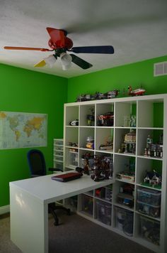 a green room with a white desk and shelves filled with toys on top of it