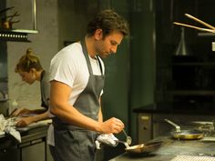 a man standing in a kitchen preparing food on top of a frying pan with tongs