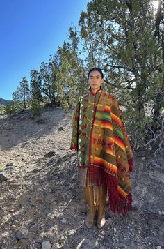 a woman standing on top of a rocky hillside wearing a colorful blanket over her head