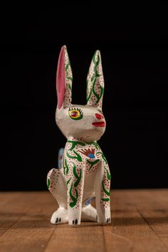 a white and green rabbit figurine sitting on top of a wooden table next to a black background