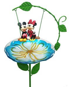 two mickey and minnie mouse figurines sitting on top of a flower with green leaves