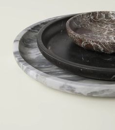 two black and white marble plates sitting on top of each other, one with a wooden bowl in the middle