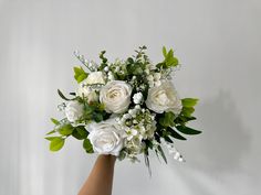 a bouquet of white roses and greenery in someone's hand on a white background