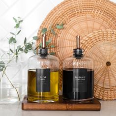 two bottles of olive oil sitting on top of a wooden tray next to a wicker basket