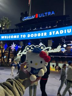 a person holding up a hello kitty stuffed animal in front of a stadium at night