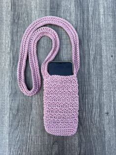 a crocheted cell phone case with a lanyard hanging from the side on a wooden surface