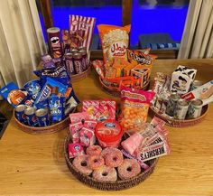 an assortment of snacks and candy in baskets on a table next to a window with curtains