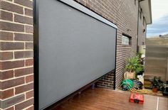 a large screen on the side of a brick building next to a planter and potted plants