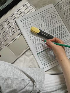 a person is holding a pen and writing on a book next to a laptop computer